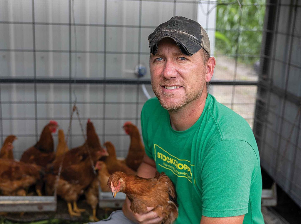 man with baseball cap holding chicken in chicken coop