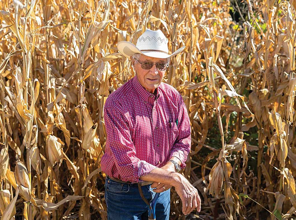 man with cowboy hat and sunglasses kneeling in corn field