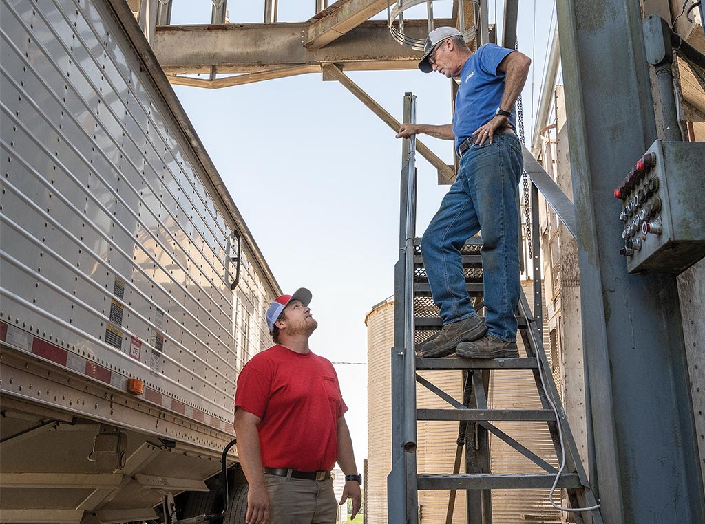 person looking up at person on ladder next to tractor trailer