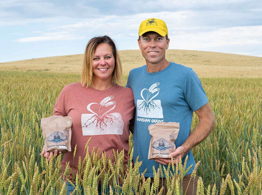 man and woman standing in wheat field in front of hill