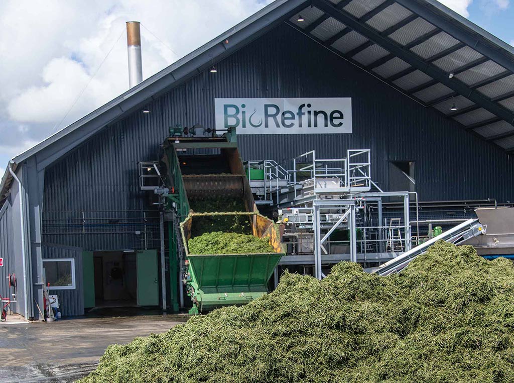 hill of fresh cut grass in front of protein processing plant