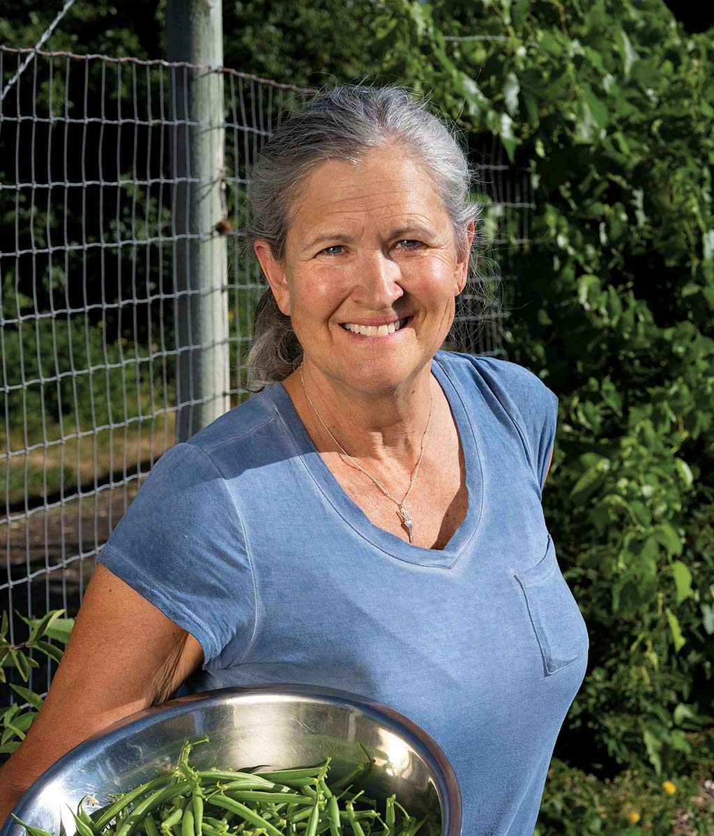 woman smiling with metal bowl of green beans in arm