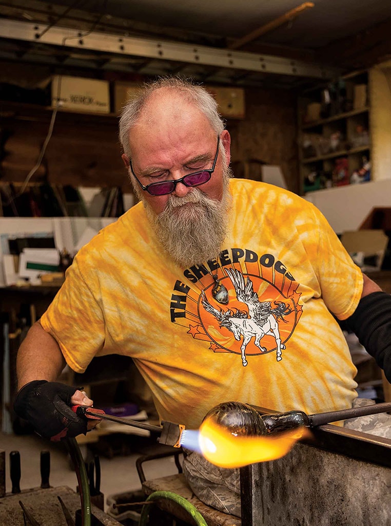 man torching glass bulb to shape it