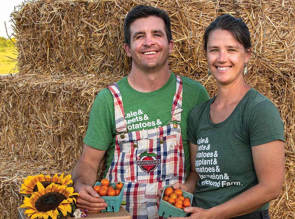 man and woman smiling in front of hay bales with containers of cherry tomatoes