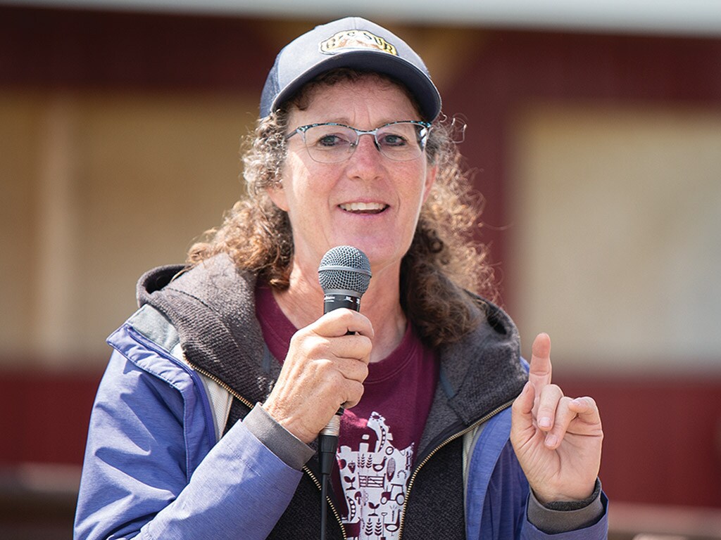 person with glasses and baseball hat speaking into a microphone