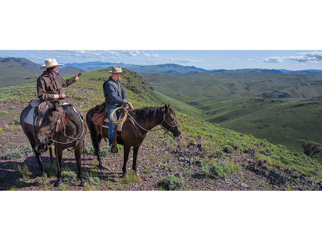 two people on horseback overlooking mountains and valleys