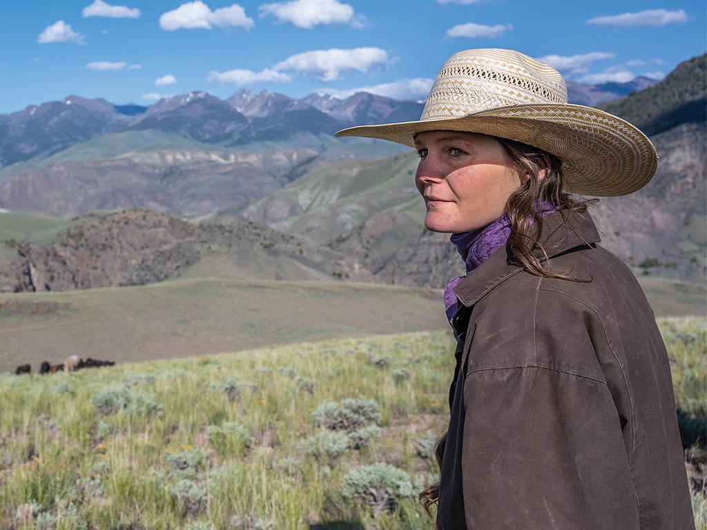 young woman with wide brimmed hat looking out at mountains