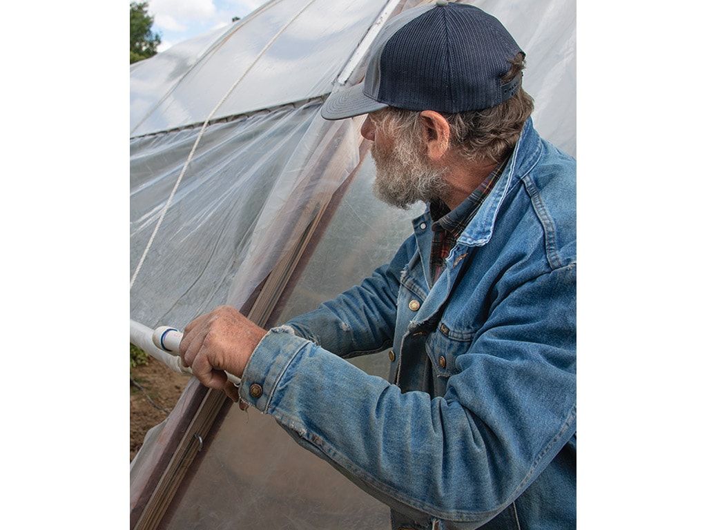 a person handling plastic piping next to a greenhouse