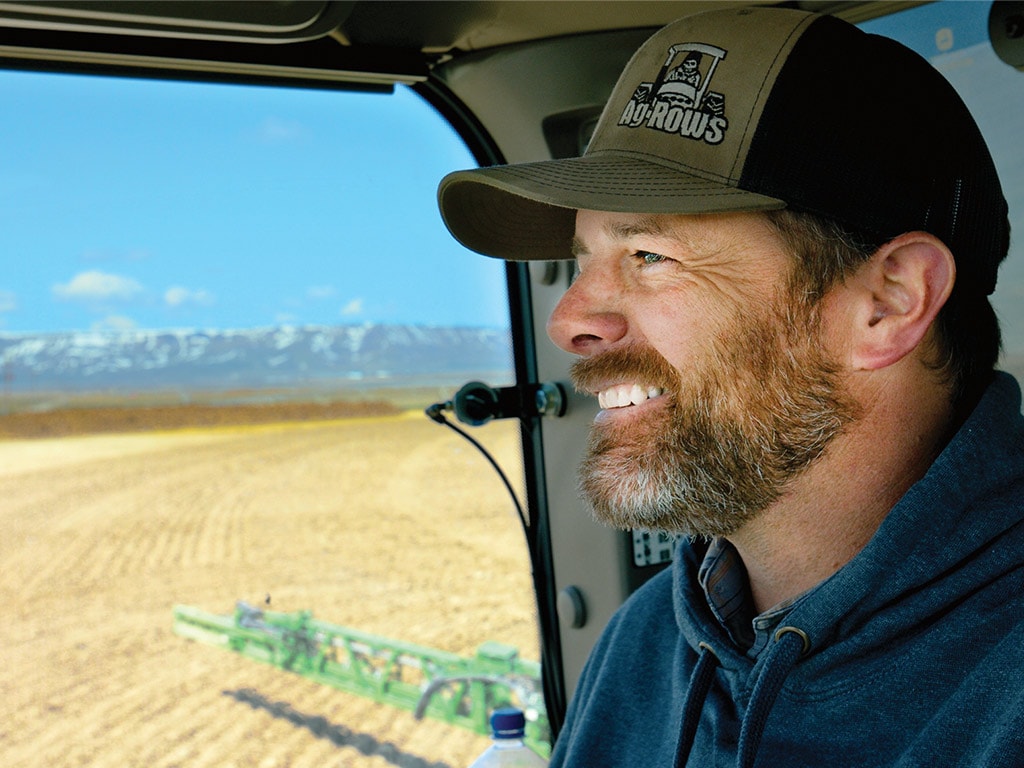 Person smiling in the cab of machine with a field and mountains in the background