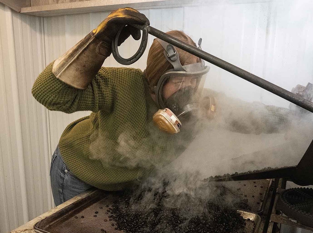 woman with gas mask and long gloves on tending to coffee bean roaster