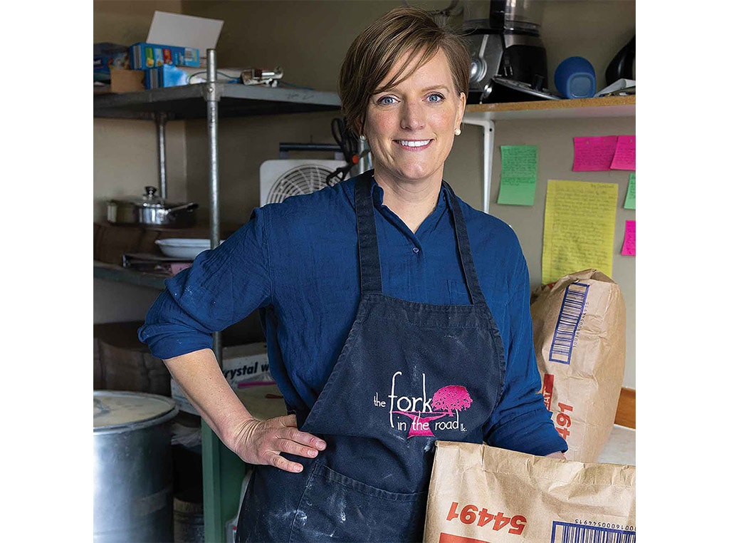 a woman with blue shirt and black apron on surrounded by shelving