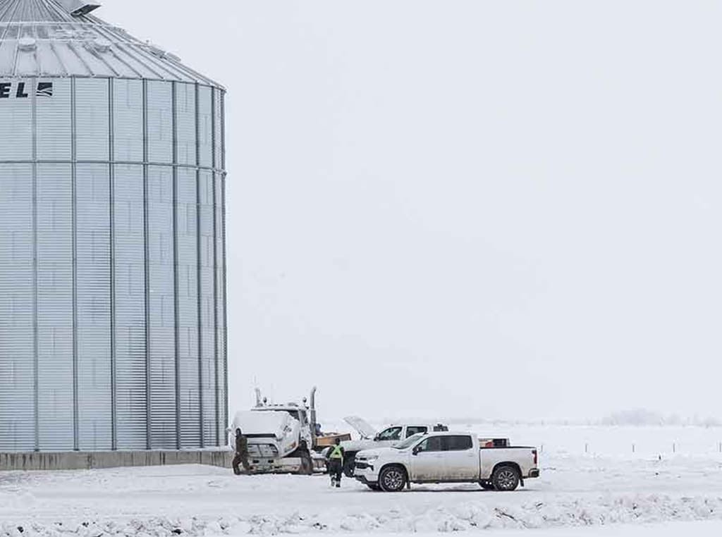 pickup trucks parked in the snow next to metal silo