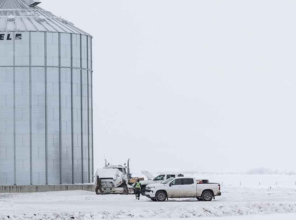 pickup trucks parked in the snow next to metal silo