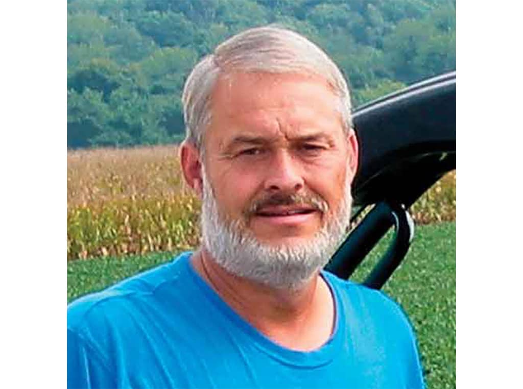 grey haired man with beard and turquoise shirt smiling