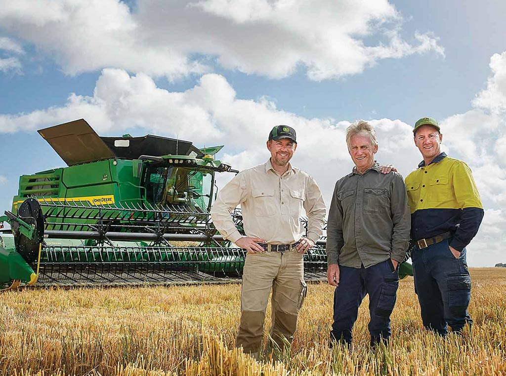 three men standing in field in front of a John Deere combine