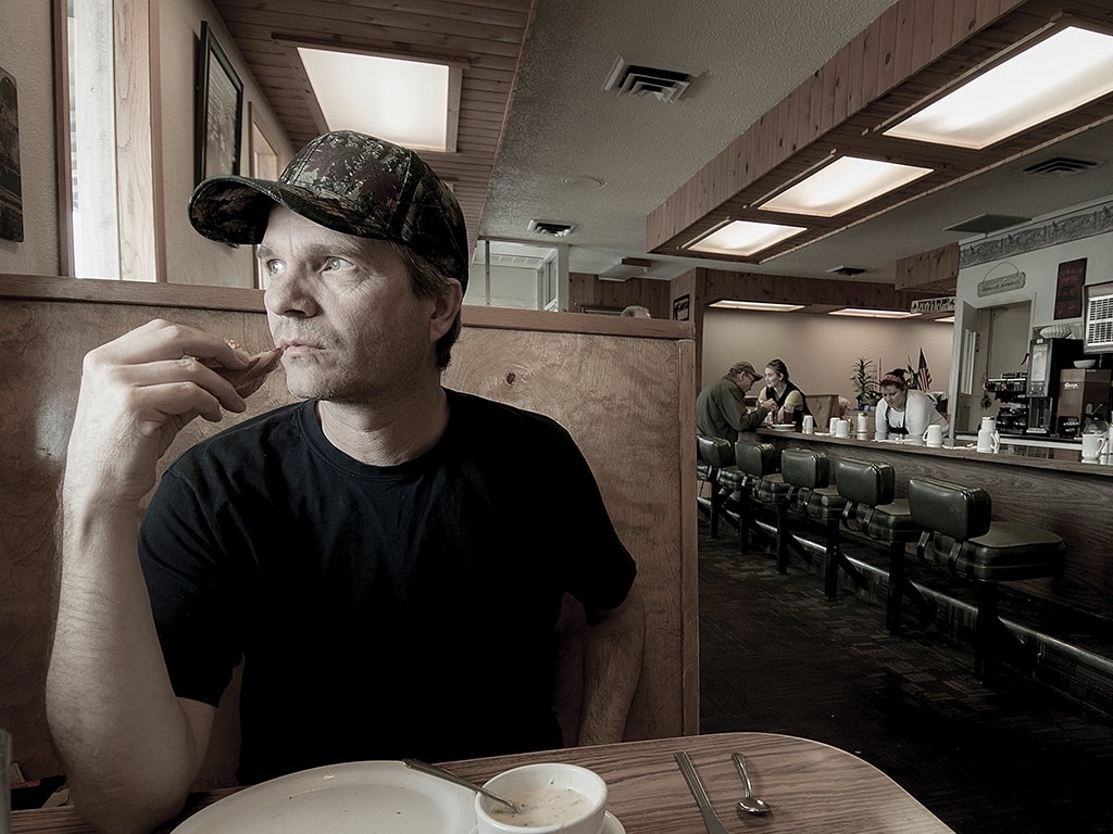 Person with baseball cap and tshirt sitting at a booth in a diner