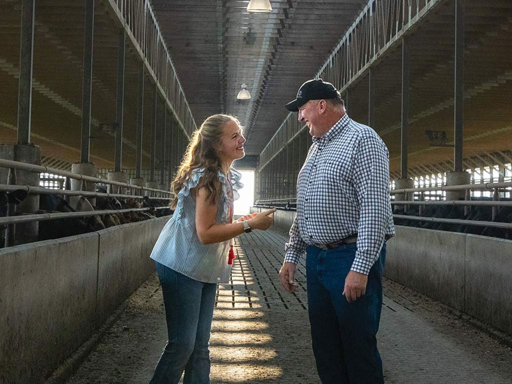 Two farmers smiling at each other in a livestock barn