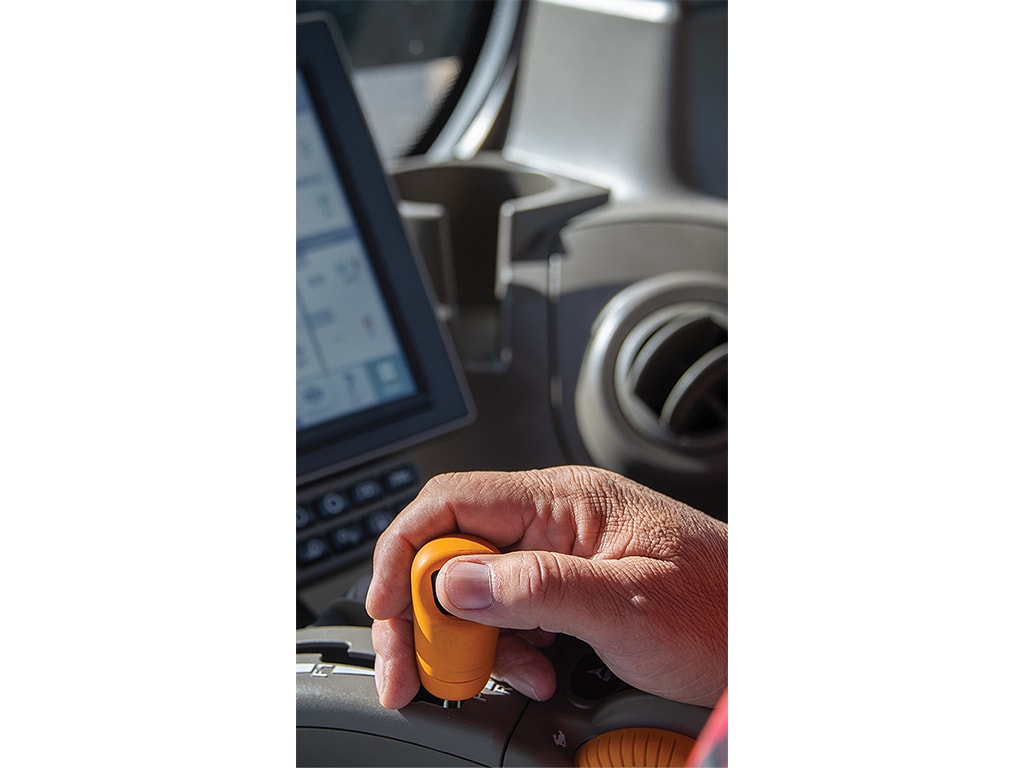 closeup of a hand holding an orange joystick in a tractor cab