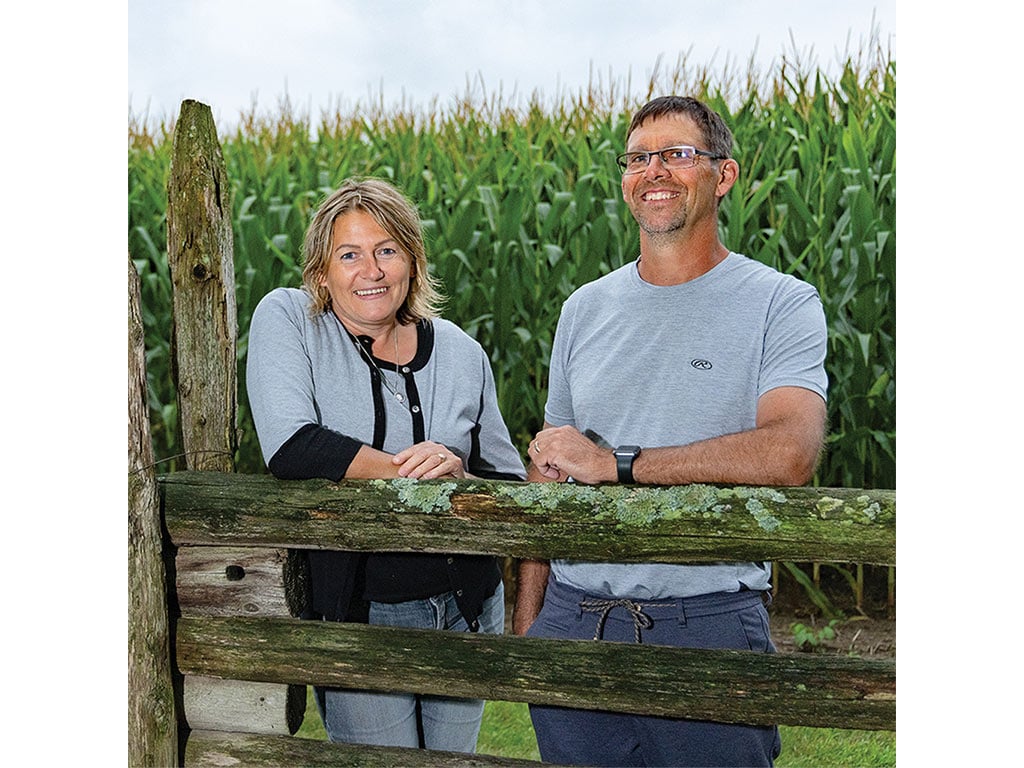 Two people leaning on a fence in front of corn stalks