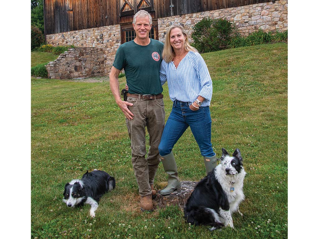 A couple stands together with their dogs outside on grass