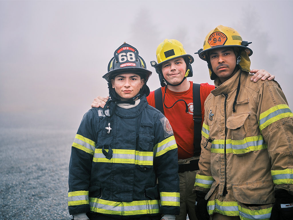 Three volunteer firefighters in uniform surrounded by smoke