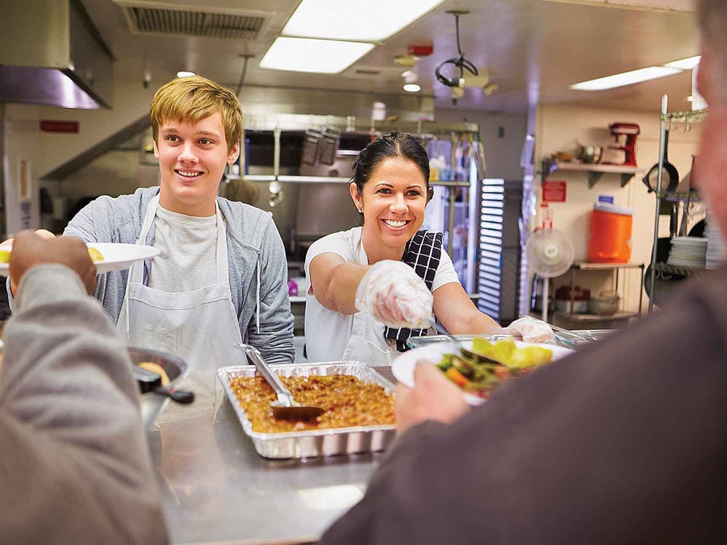 Two people serving trays of food to two others at a food bank