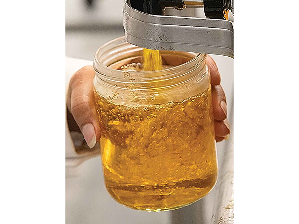 golden liquid clarified butter pouring into a glass jar 