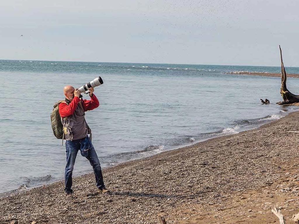 a photographer on a beach pointing their camera up to the right away from the water