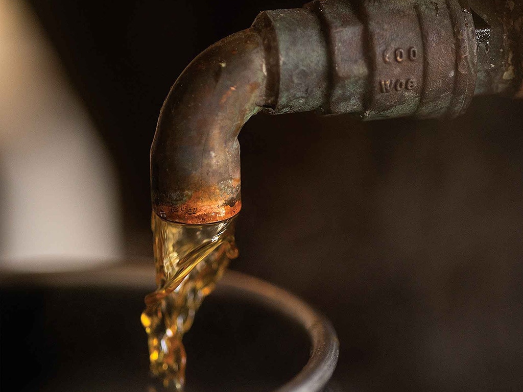 Closeup of a faucet pouring syrup into a metal container