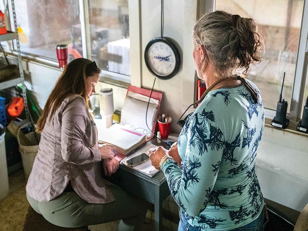 two people in an office looking at a three ring binder