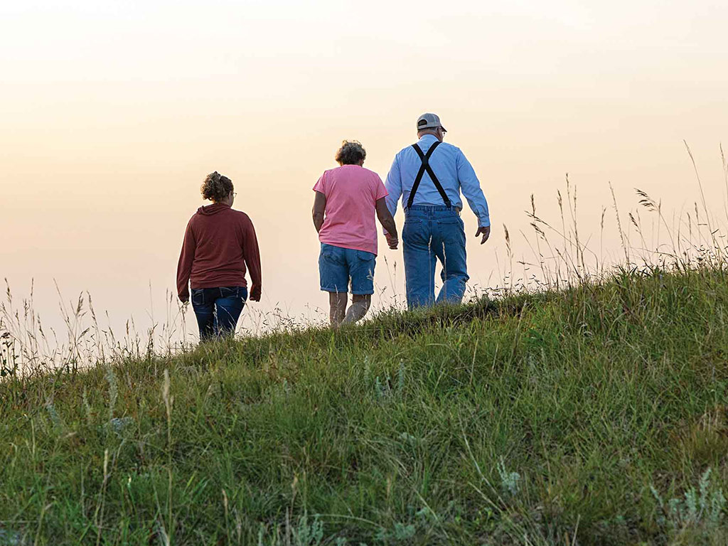 three people walking over a hilltop into a dusky distance