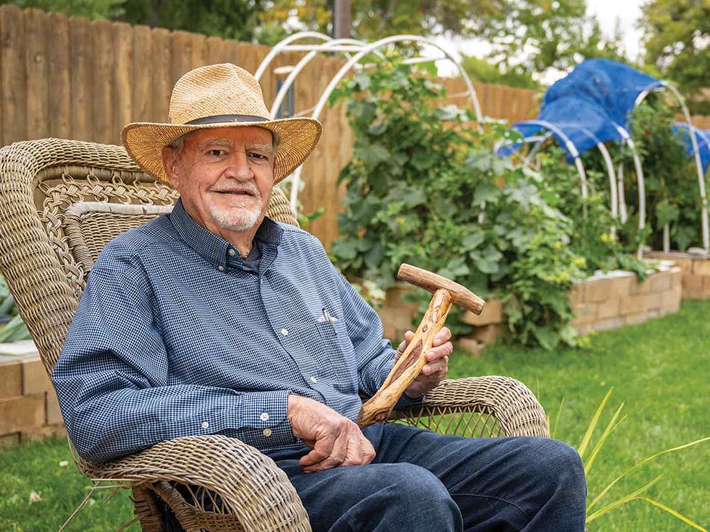 a smiling farmer sitting outside presenting a wooden planting tool