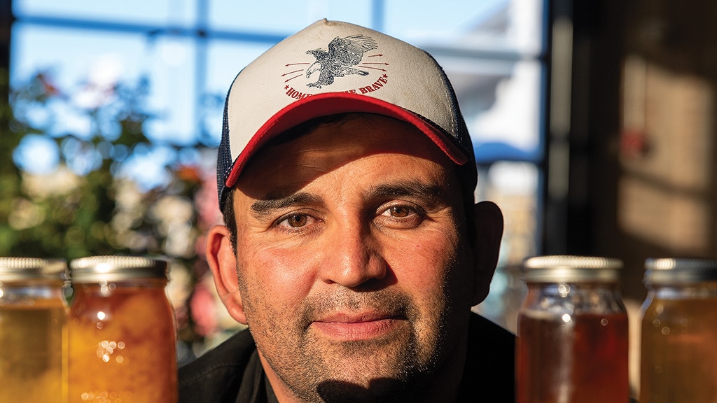 closeup of smiling person with baseball cap on surrounded by jars of honey