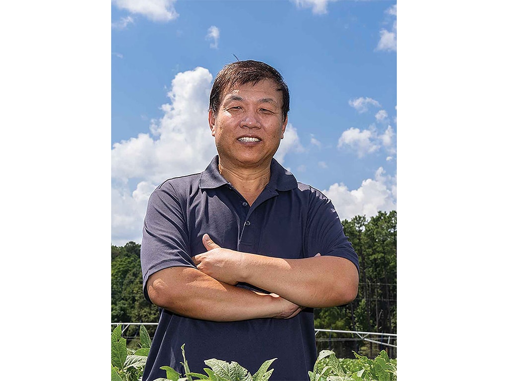 smiling person standing in field with arms crossed