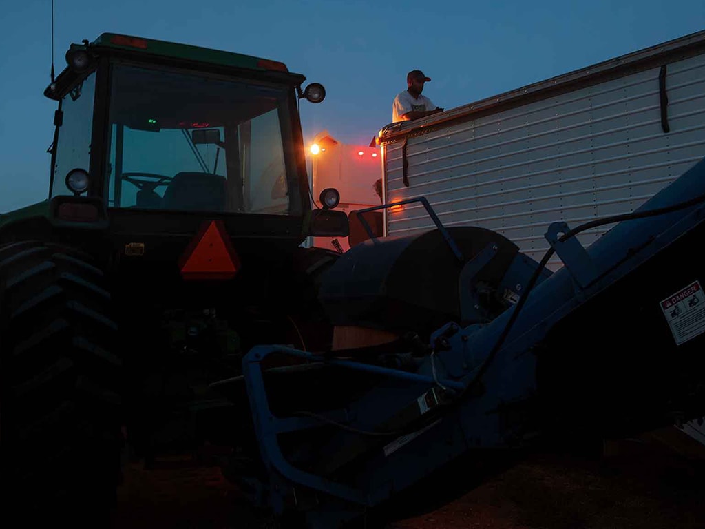 Farm worker on top of a tractor trailer with John Deere tractor in the foreground