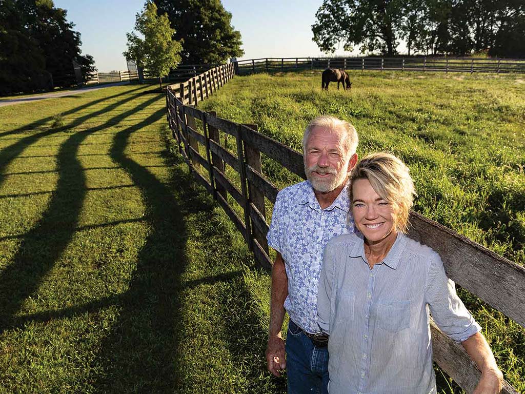 Two smiling farmers leaning on a horse fence with a horse grazing in a field in the background