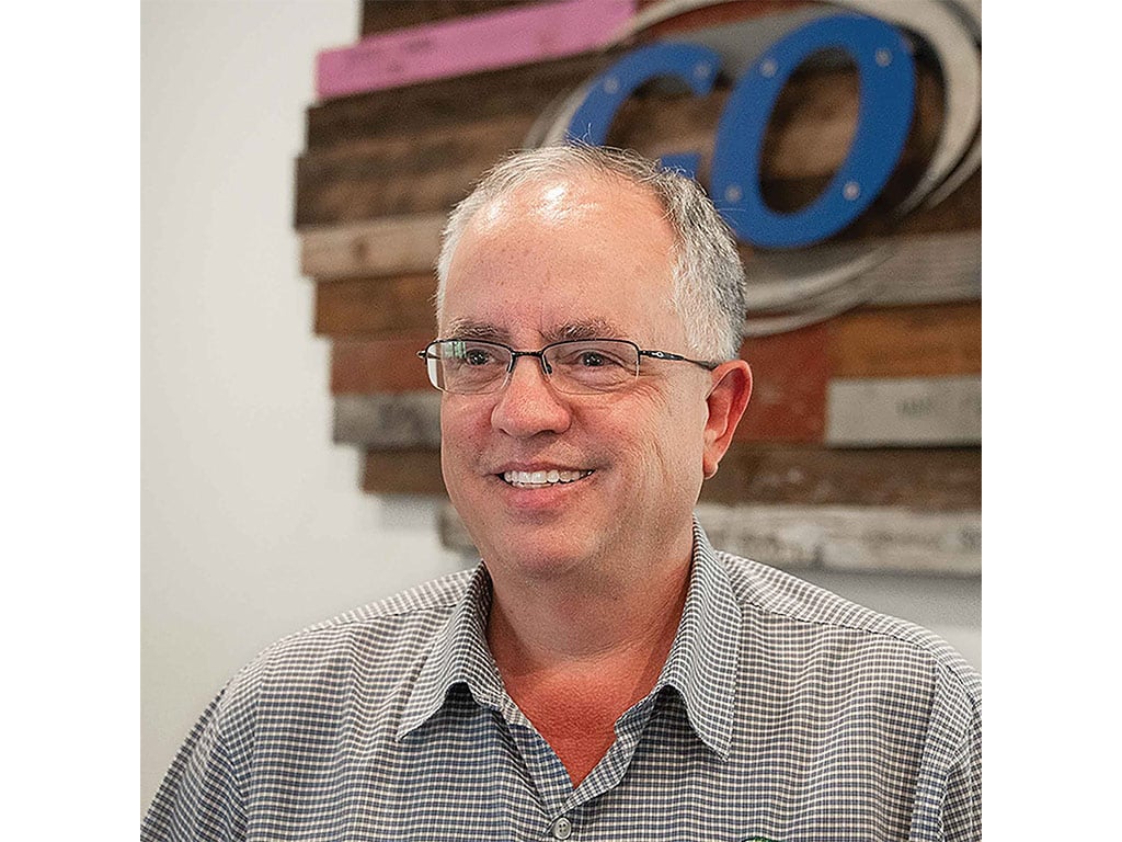 smiling person wearing glasses and grey button-down shirt