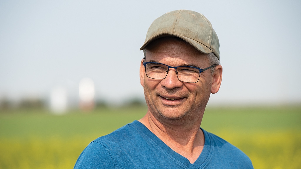 smiling person with baseball cap, eyeglasses, and blue tshirt