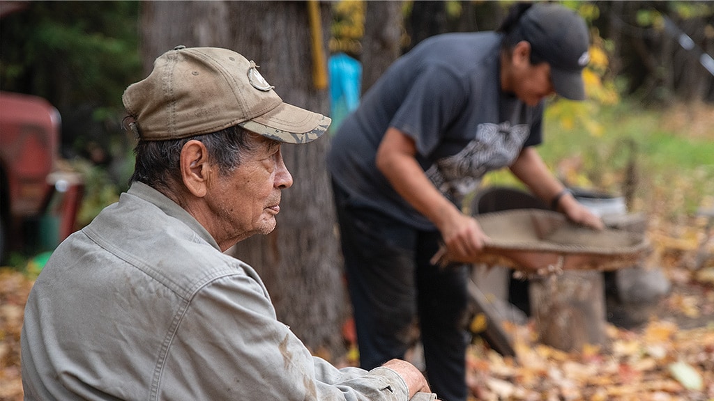 man with light brown cap looking side ways and in a distant out of focus man seen