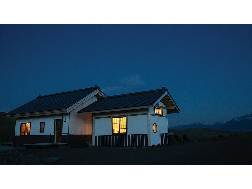 A Japanese farmhouse with mountains in the distance at either dusk or dawn