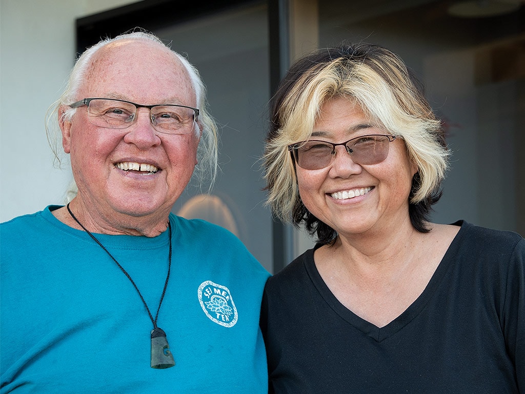 A smiling couple wearing glasses standing in front of sliding glass doors