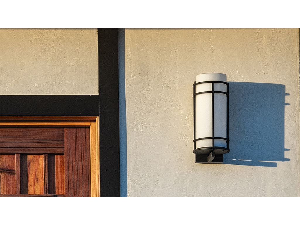 The top right corner of a wooden door and a black and white outdoor sconce light fixture