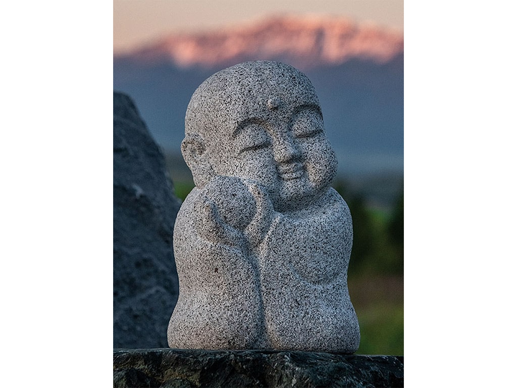A stone sculpture of the Japanese god, Jizō, with blurred mountains in the background