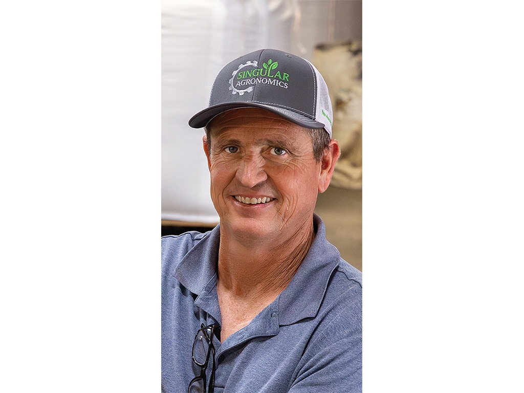 A smiling person with a baseball cap on that reads Singular Agronomics