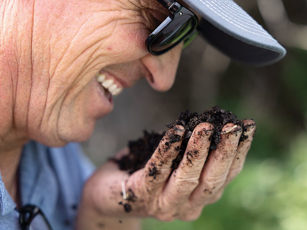 A profile of a smiling person smelling a handful of soil