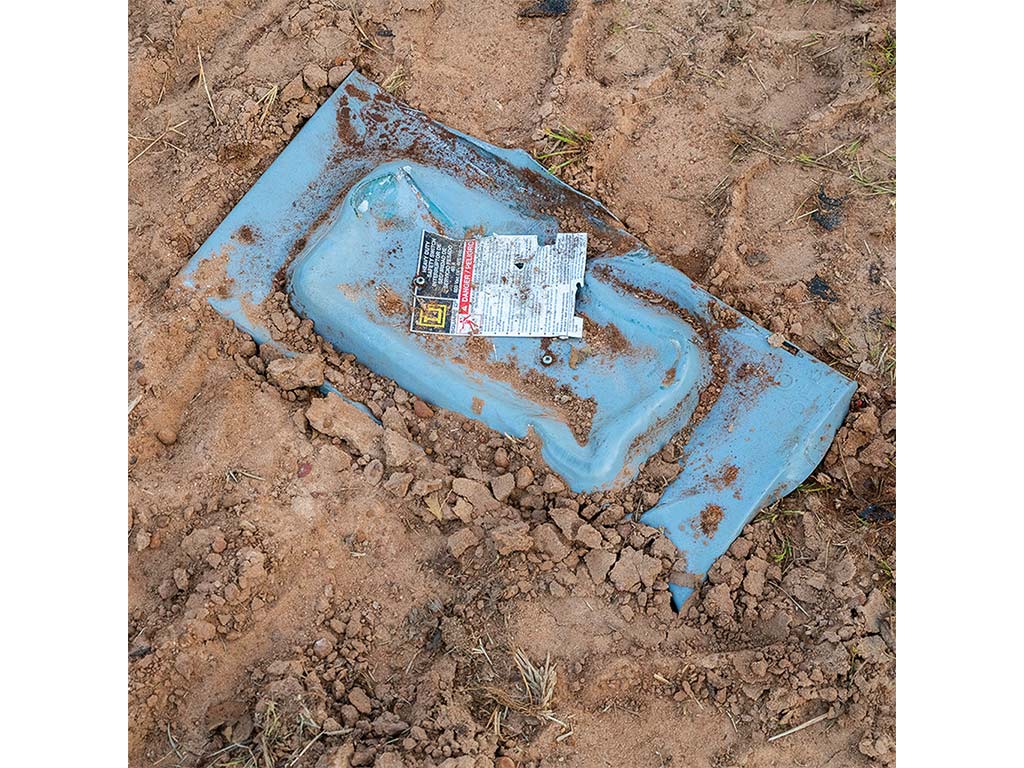 Closeup of a light blue metal object partially buried under dried mud