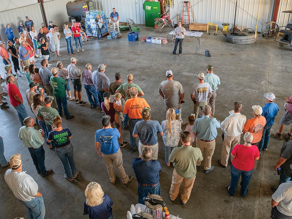A group of people standing circled around a speaking person in a warehouse