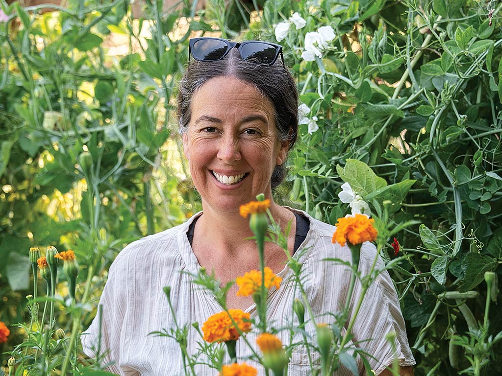 A smiling gardener standing among various plants with yellow-orange flowers