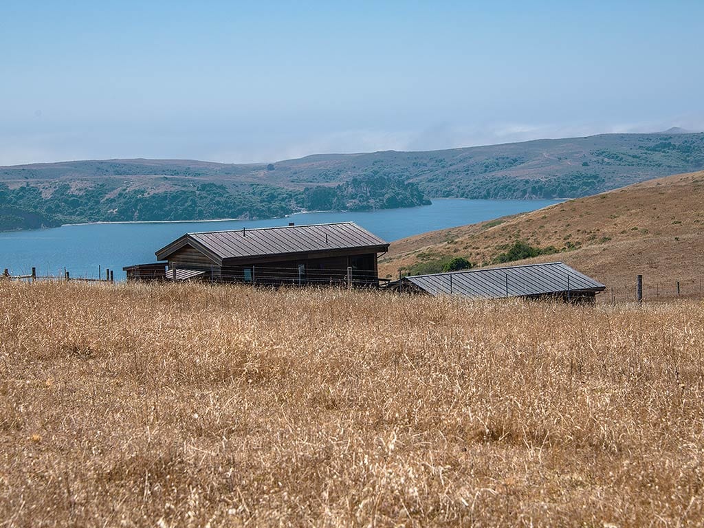 A farmhouse on a hilltop overlooking a bay.