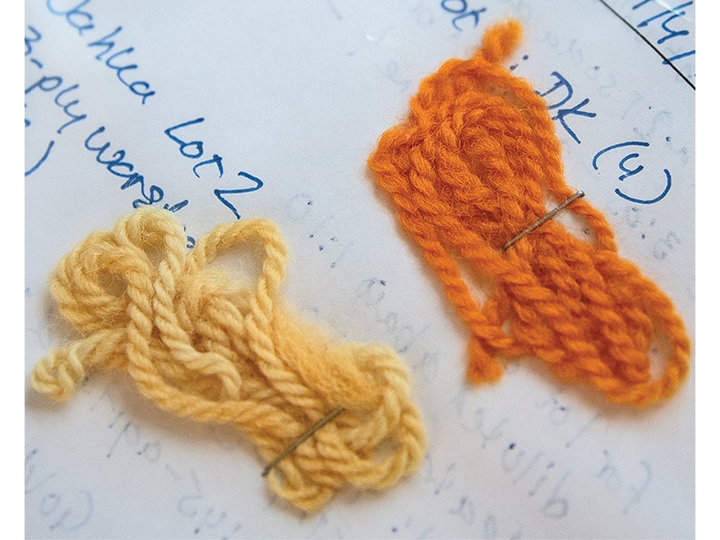 Two yarn samples, yellow on the left and orange on the right, stapled to a piece of paper with notes on it.
